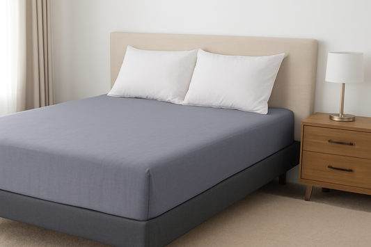 A cozy bedroom featuring a gray fitted bed sheet, white pillows, and a wooden nightstand.
