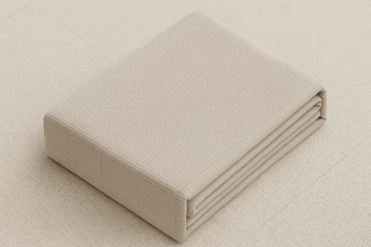 Folded beige fitted bed sheet with subtle grid texture on matching fabric background, viewed horizontally.
