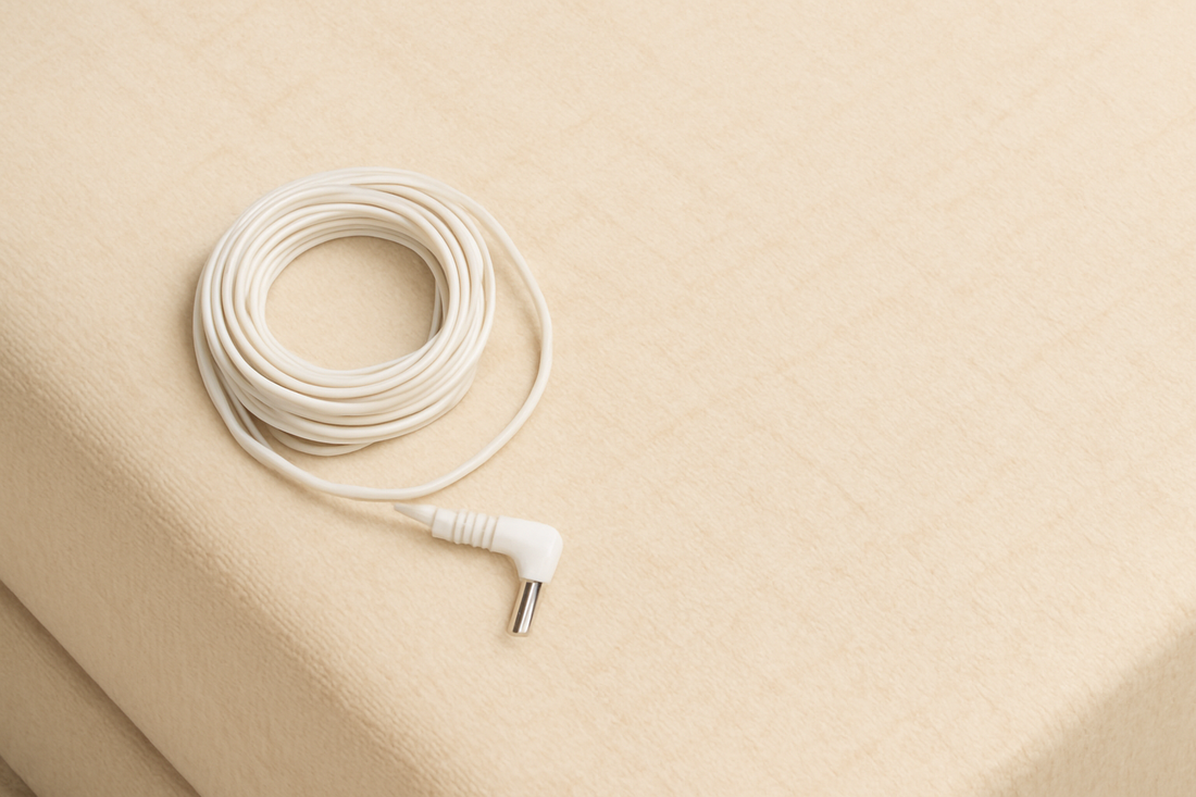 A beige grounding sheet draped over a mattress with a coiled white grounding cable beside it.