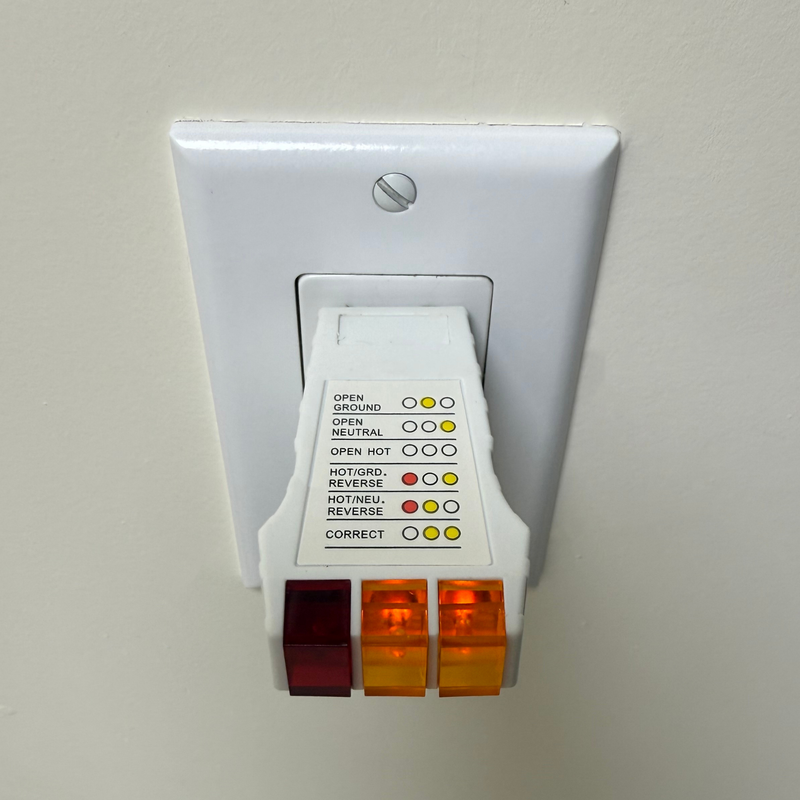 Groundluxe grounding outlet checker plugged into a wall outlet showing the two orange lights illuminated which indicated the outlet is properly grounded.