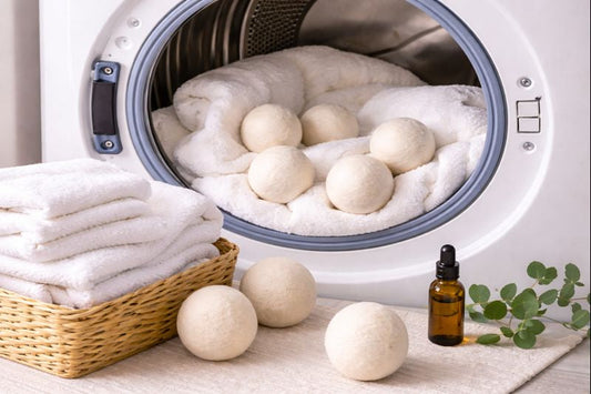 Wool dryer balls resting on white towels inside an open front-loading dryer with neatly folded laundry nearby.