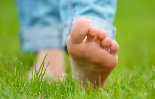 A bare foot stepping in the grass. Person is wearing jeans.