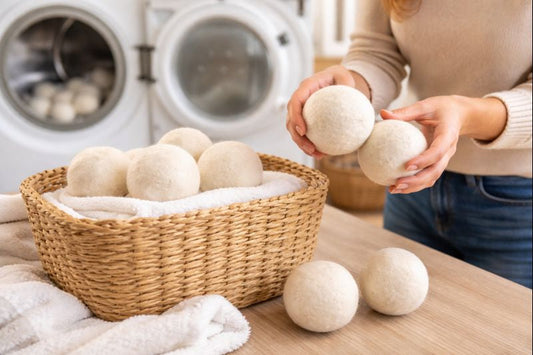 Woman examining wool dryer balls beside a laundry basket in a bright laundry room with dryer in background.