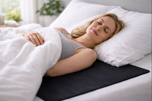 Woman sleeping peacefully on a pure black grounding mat in a bright bedroom with soft white bedding.