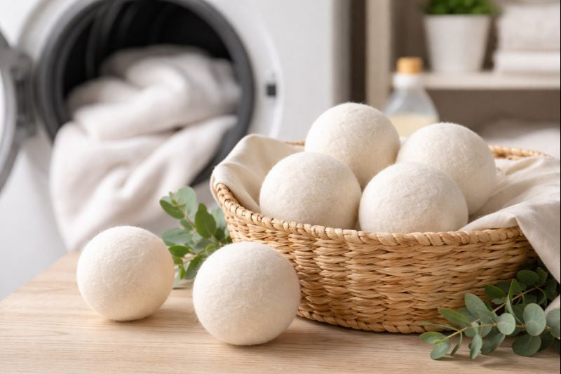 Wool dryer balls in a wicker basket beside a dryer, shown in a clean and natural laundry setting.
