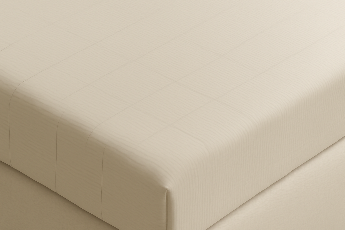 Close-up of a bed with a beige fitted grounding sheet, neatly stretched over the mattress corner.