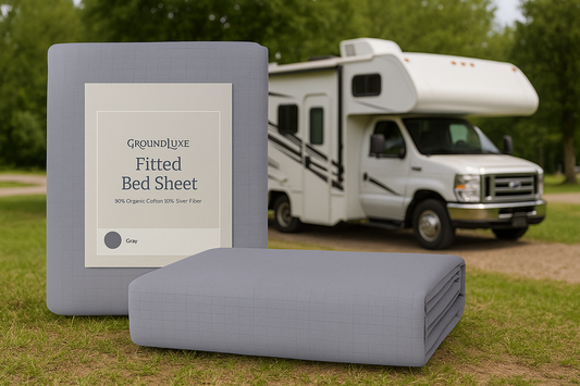 Gray GroundLuxe fitted bed sheet beside an RV on grass with forest background, captured in daylight.