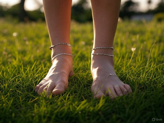 Bare feet with anklets standing on lush green grass at sunset.