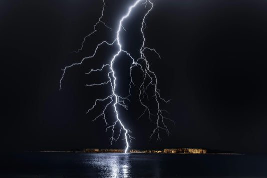 Bright lightning bolt striking over water at night with dark sky