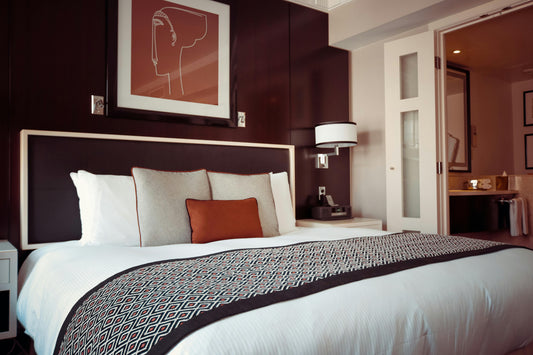 Modern hotel bedroom with a neatly made bed, decorative pillows, elegant lighting, and a framed artwork