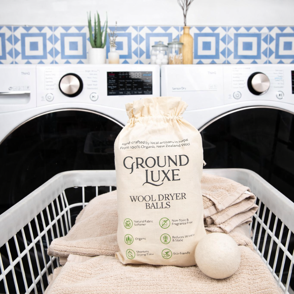 Bag of Ground Luxe wool dryer balls in front of a washing machine with a dryer.

